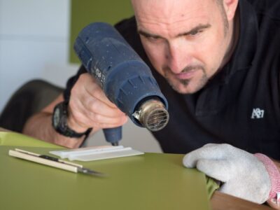 Mann erhitzt grüne Folie mit Heissluftföhn.